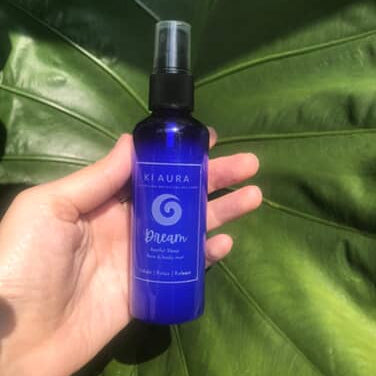 Hand holding a blue bottle labeled 'Mylaura' against a green leafy background