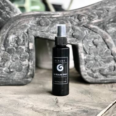 Black spray bottle labeled 'K'aura' on a stone surface with decorative background